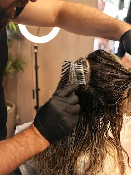 Le mani della colorista stendono il colore su una ciocca con il pettine